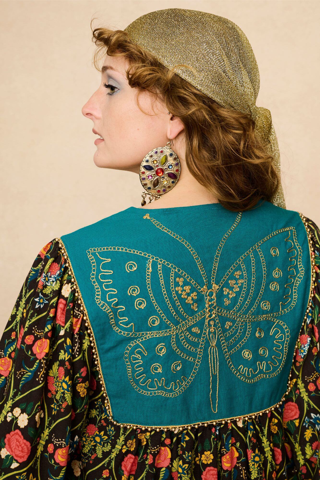 Model wearing a 70s style floral mini dress and matching boots against a beige background - back view close up