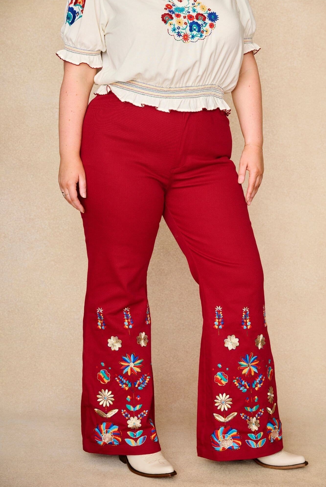 Model wears red flared trousers by The Hippie Shake, crafted from soft cotton twill with a gentle stretch, adorned with glowing floral vines and golden lurex - close up view