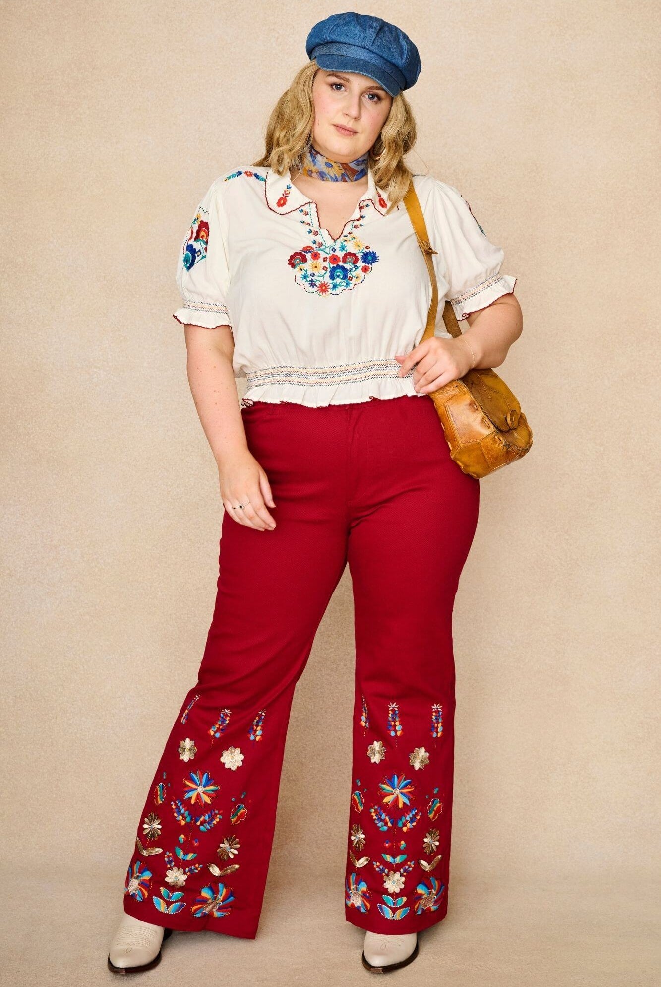 Model wears red flared trousers by The Hippie Shake, crafted from soft cotton twill with a gentle stretch, adorned with glowing floral vines and golden lurex.