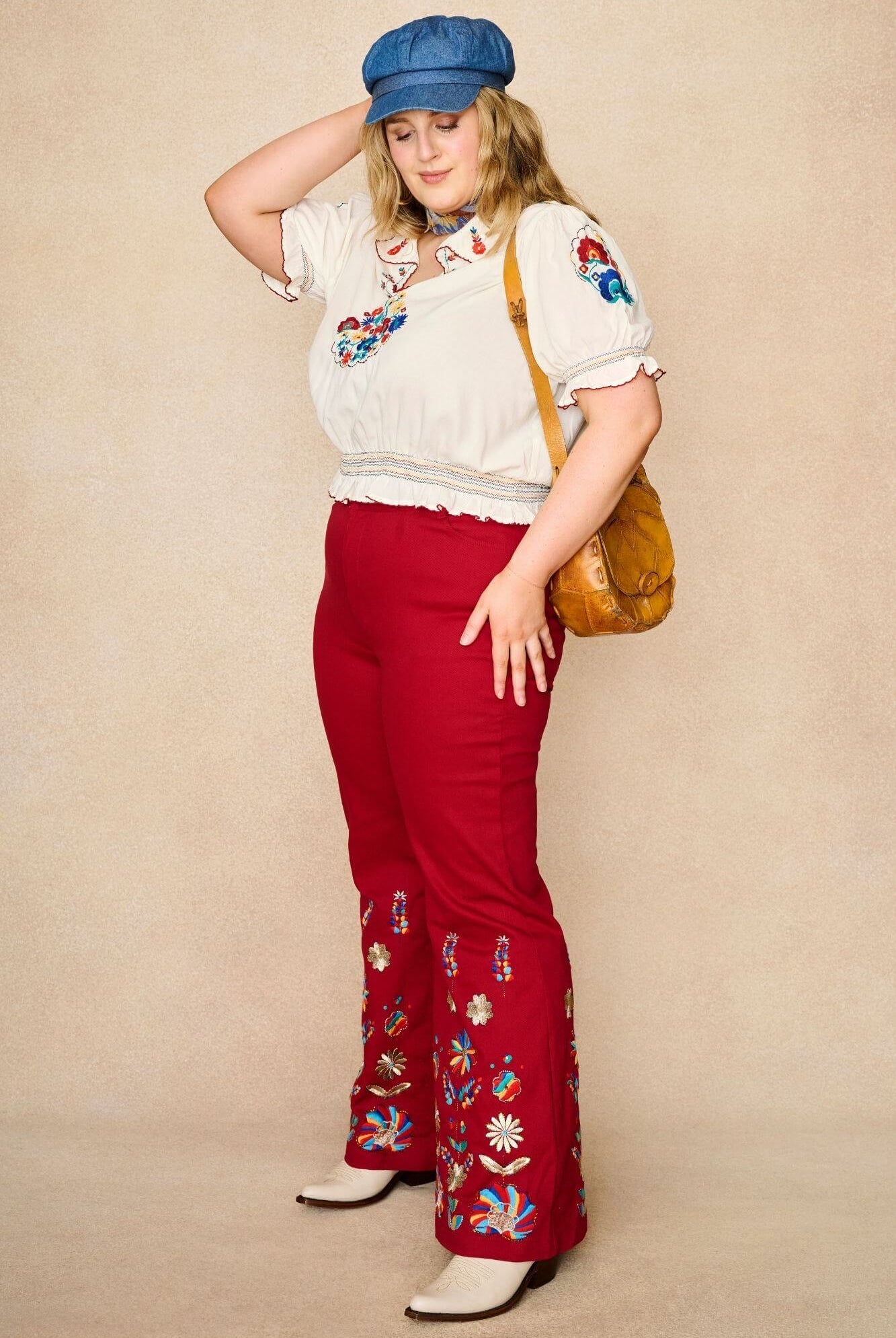 Model wears red flared trousers by The Hippie Shake, crafted from soft cotton twill with a gentle stretch, adorned with glowing floral vines and golden lurex - standing side view