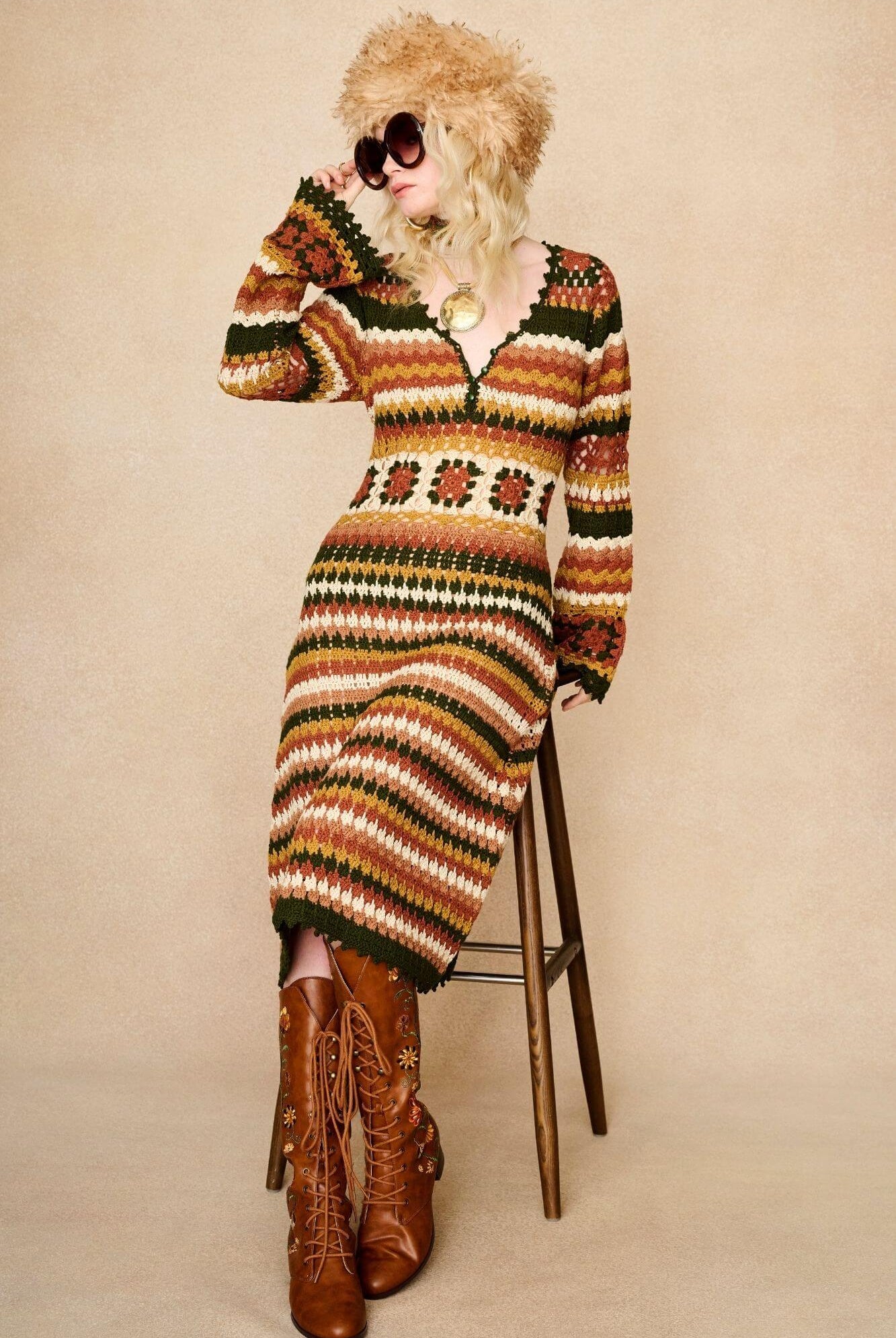 Model wears striped crochet midi dress hand crocheted in cotton with 70s-inspired detailing by The Hippie Shake. Seated on chair front view