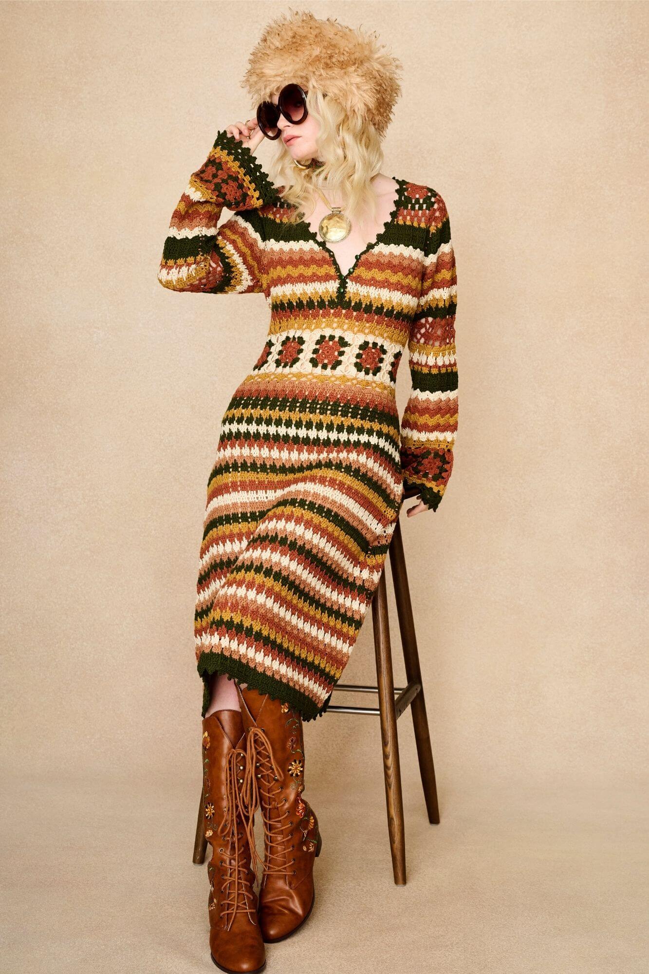Model wears striped crochet midi dress hand crocheted in cotton with 70s-inspired detailing by The Hippie Shake. Seated on chair front view
