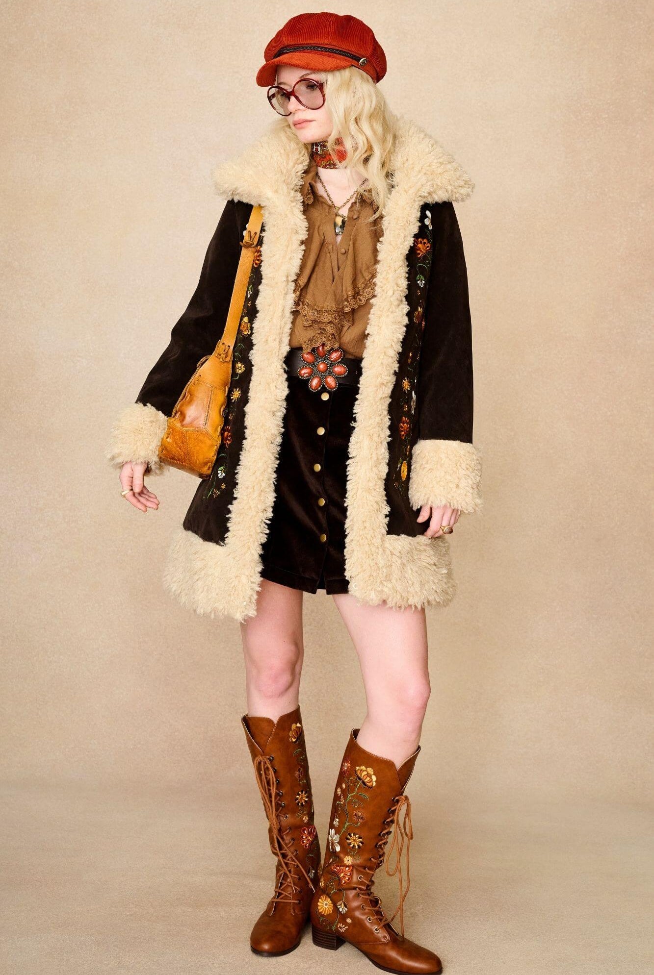 Model standing wears dark brown embroidered Penny Lane coat in faux suede with faux fur trim. A 70s-inspired statement coat made for bold, vintage boho styling by The Hippie Shake