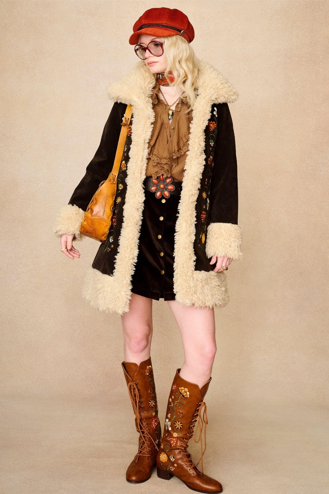Model standing wears dark brown embroidered Penny Lane coat in faux suede with faux fur trim. A 70s-inspired statement coat made for bold, vintage boho styling by The Hippie Shake