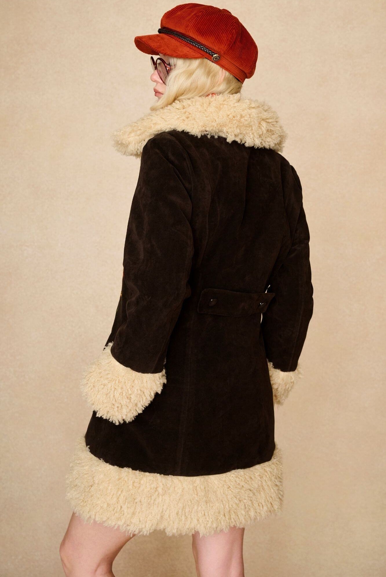 Model wears dark brown embroidered Penny Lane coat in faux suede with faux fur trim. A 70s-inspired statement coat made for bold, vintage boho styling by The Hippie Shake - back view