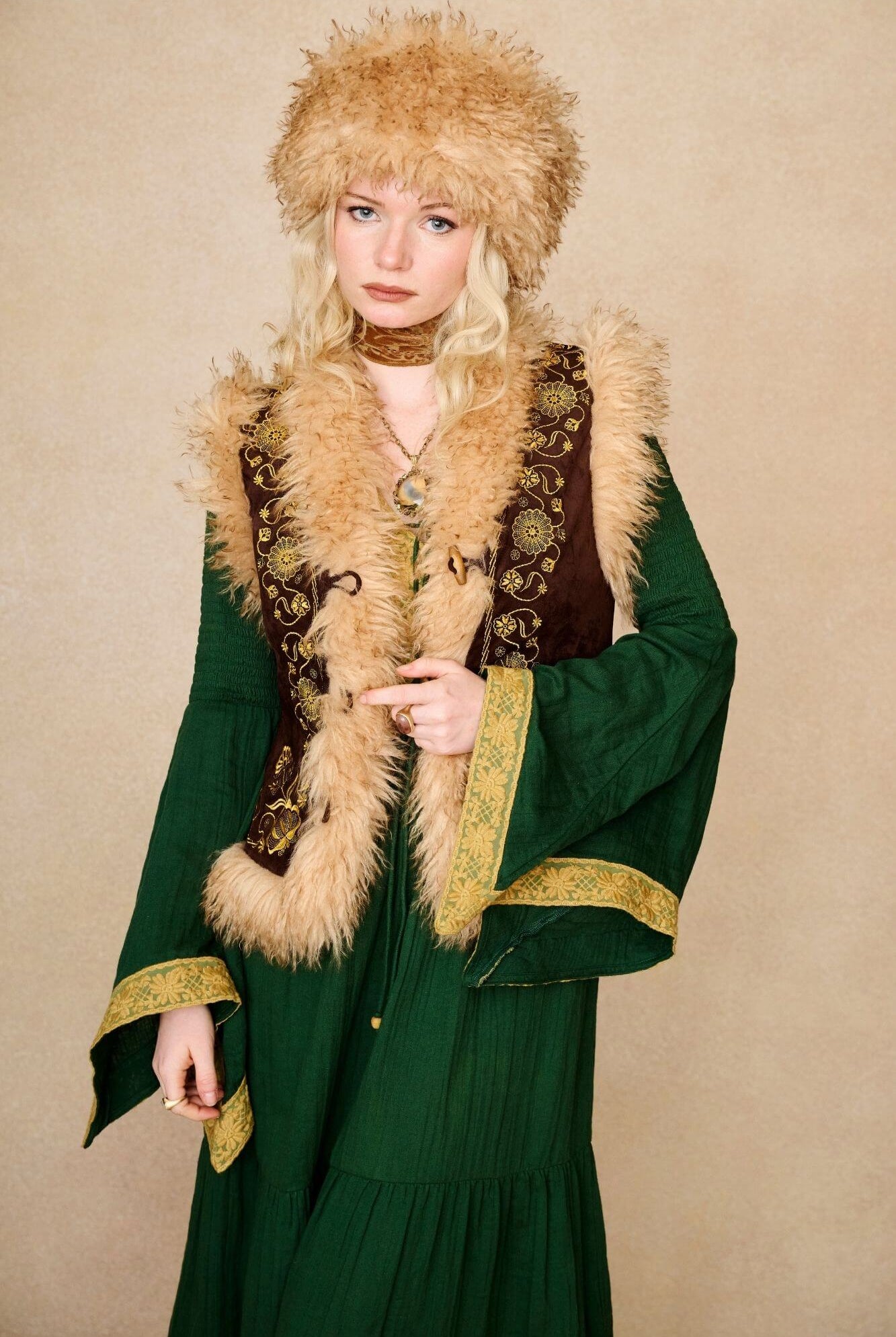 Model wears brown embroidered Penny Lane vest in faux suede with faux fur trim. A 70s-inspired boho layering piece made for vintage and festival styling by The Hippie Shake - front view paired with green dress