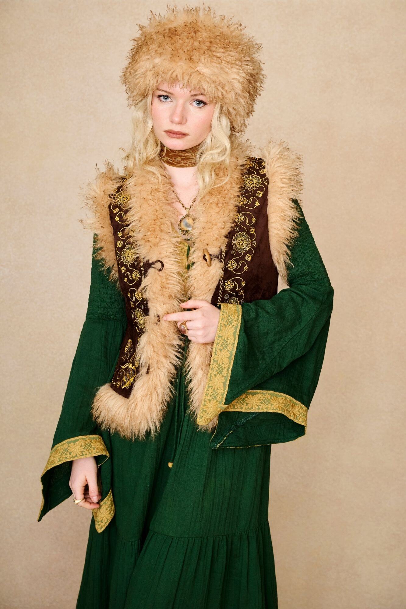 Model wears brown embroidered Penny Lane vest in faux suede with faux fur trim. A 70s-inspired boho layering piece made for vintage and festival styling by The Hippie Shake - front view paired with green dress