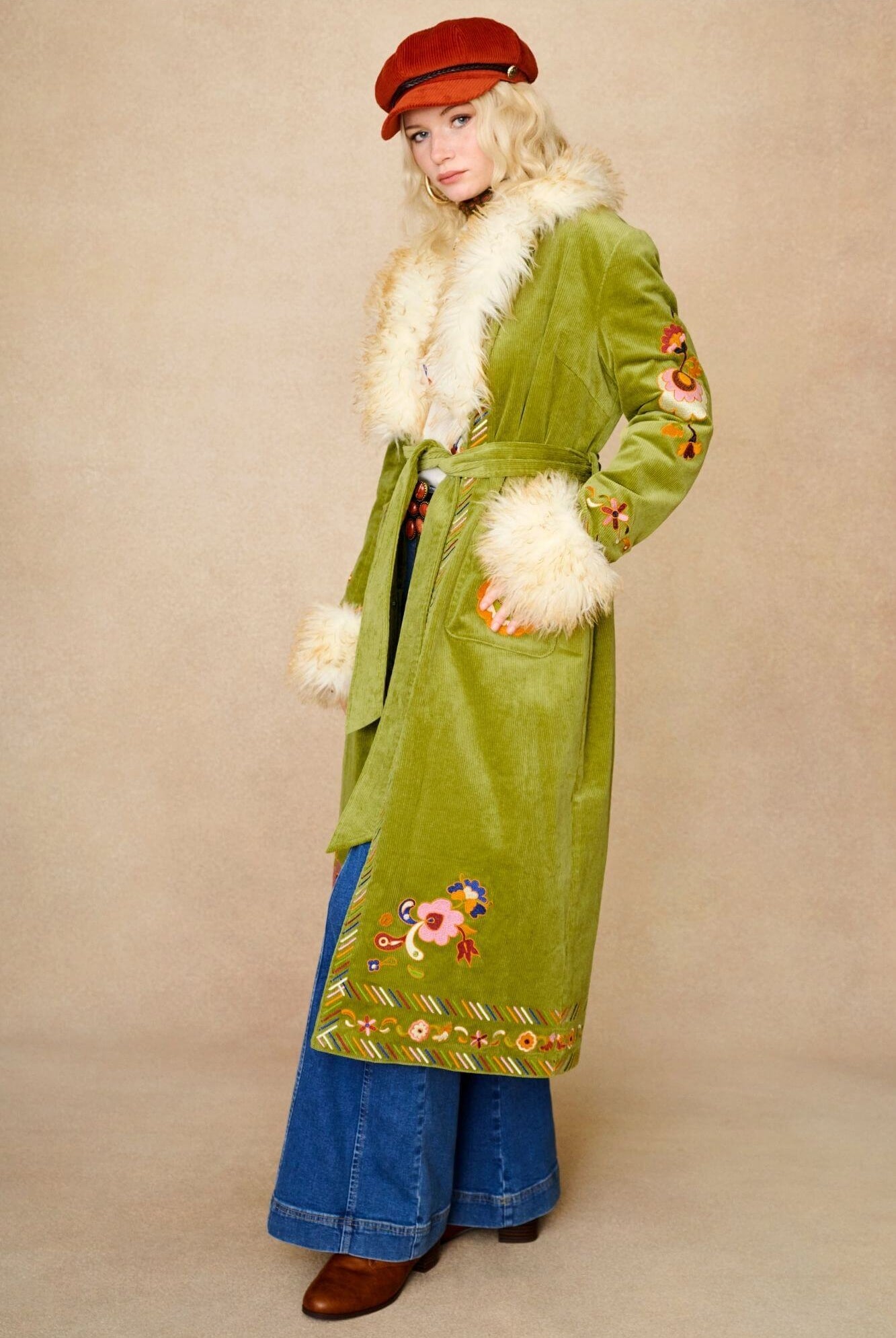 Model wears green embroidered Penny Lane coat in cotton corduroy with faux fur trim. A 70s-inspired statement coat made for bohemian, vintage styling by The Hippie Shake - closed front view with denim