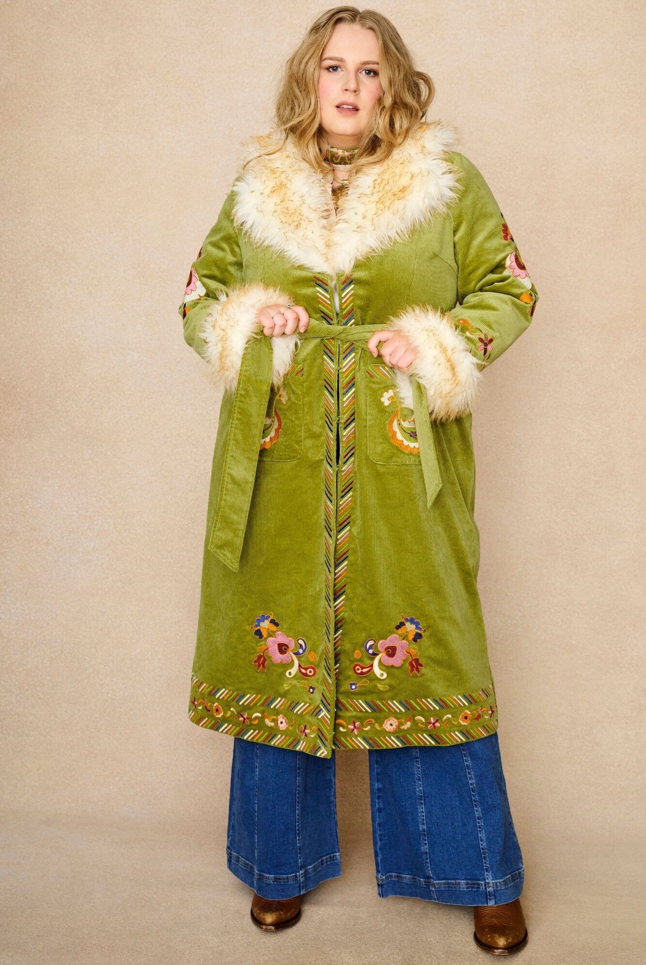 Model wears green embroidered Penny Lane coat in cotton corduroy with faux fur trim. A 70s-inspired statement coat made for bohemian, vintage styling by The Hippie Shake - wrapped front view