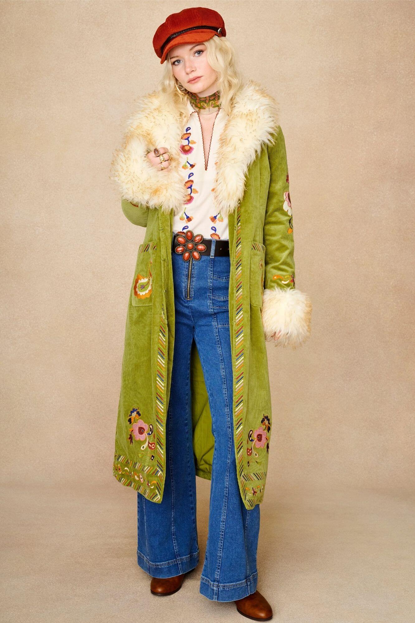 Model wears cream embroidered blouse in textured cotton with floral detailing and balloon sleeves. A 70s-inspired boho blouse made for everyday vintage styling by The Hippie Shake - paired with green Penny Lane coat