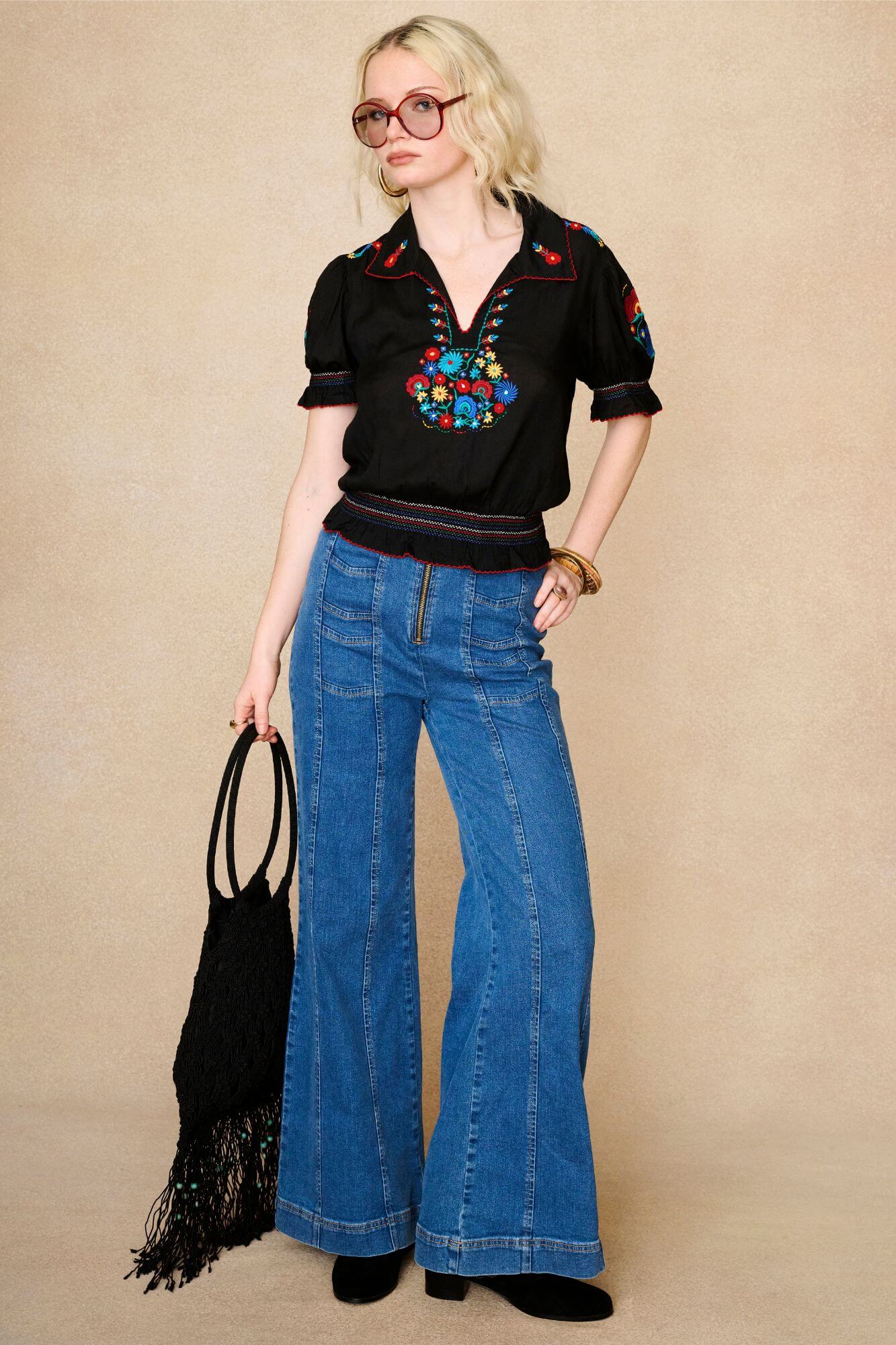 Model wears black floral embroidered blouse in soft cotton with shirred details. A vintage-inspired Penny Lane blouse made for boho, festival and everyday styling by The Hippie Shake - standing with jeans outfit