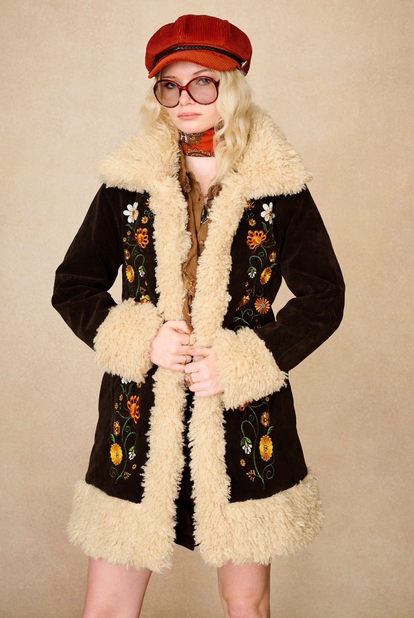 Model wears dark brown embroidered Penny Lane coat in faux suede with faux fur trim by The Hippie Shake. A 70s-inspired statement coat made for bold, vintage boho styling.