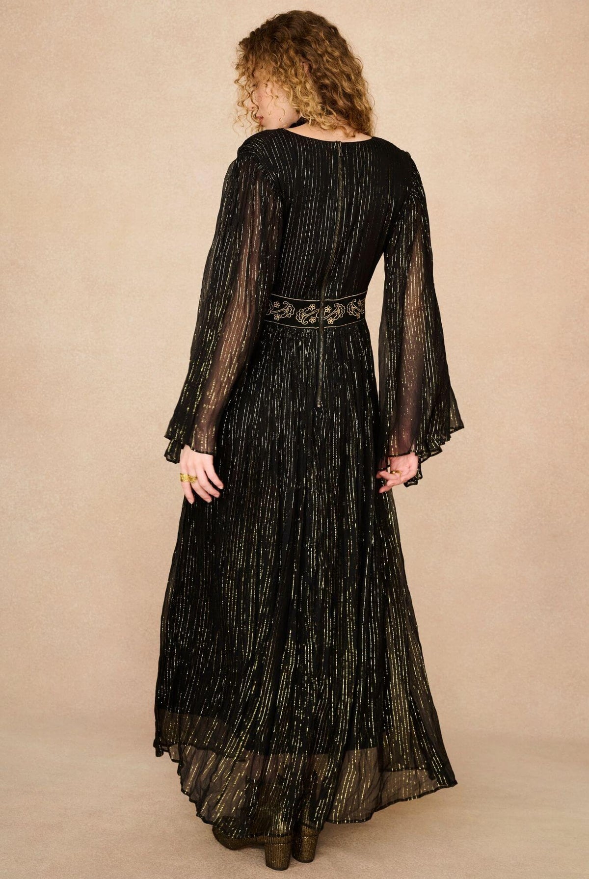 A model wearing a black maxi dress with sheer long flowy sleeves by the Hippie Shake