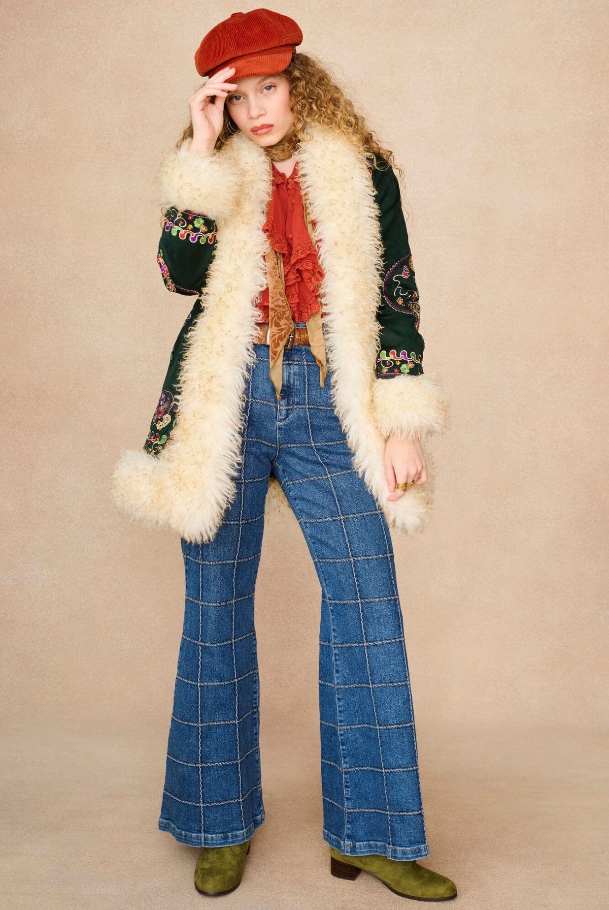 A model wearing a 1970s style outfit featuring a dark green embroidered jacket with a cream faux fur collar.