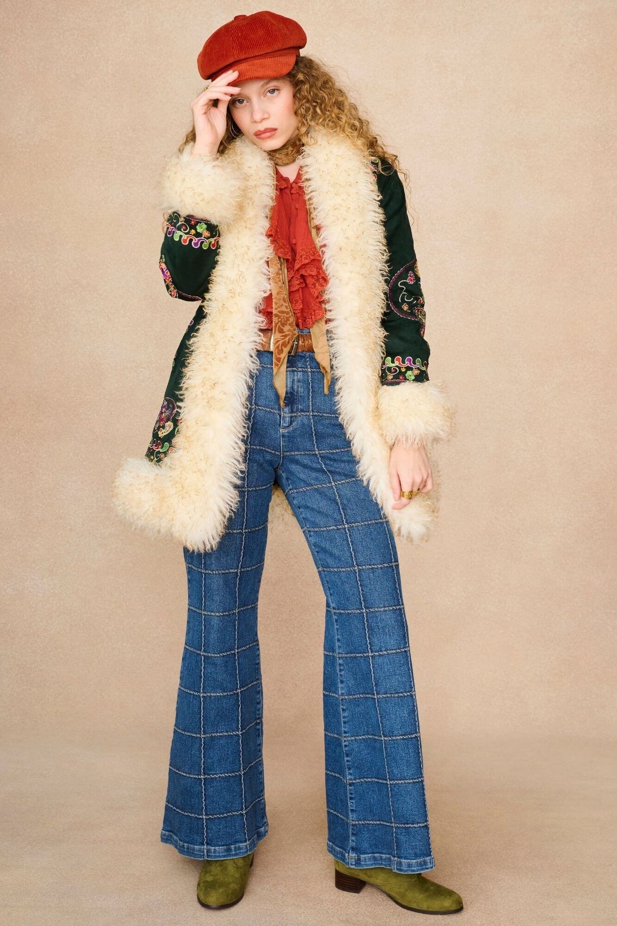A model wearing a 1970s style outfit featuring a dark green embroidered jacket with a cream faux fur collar.