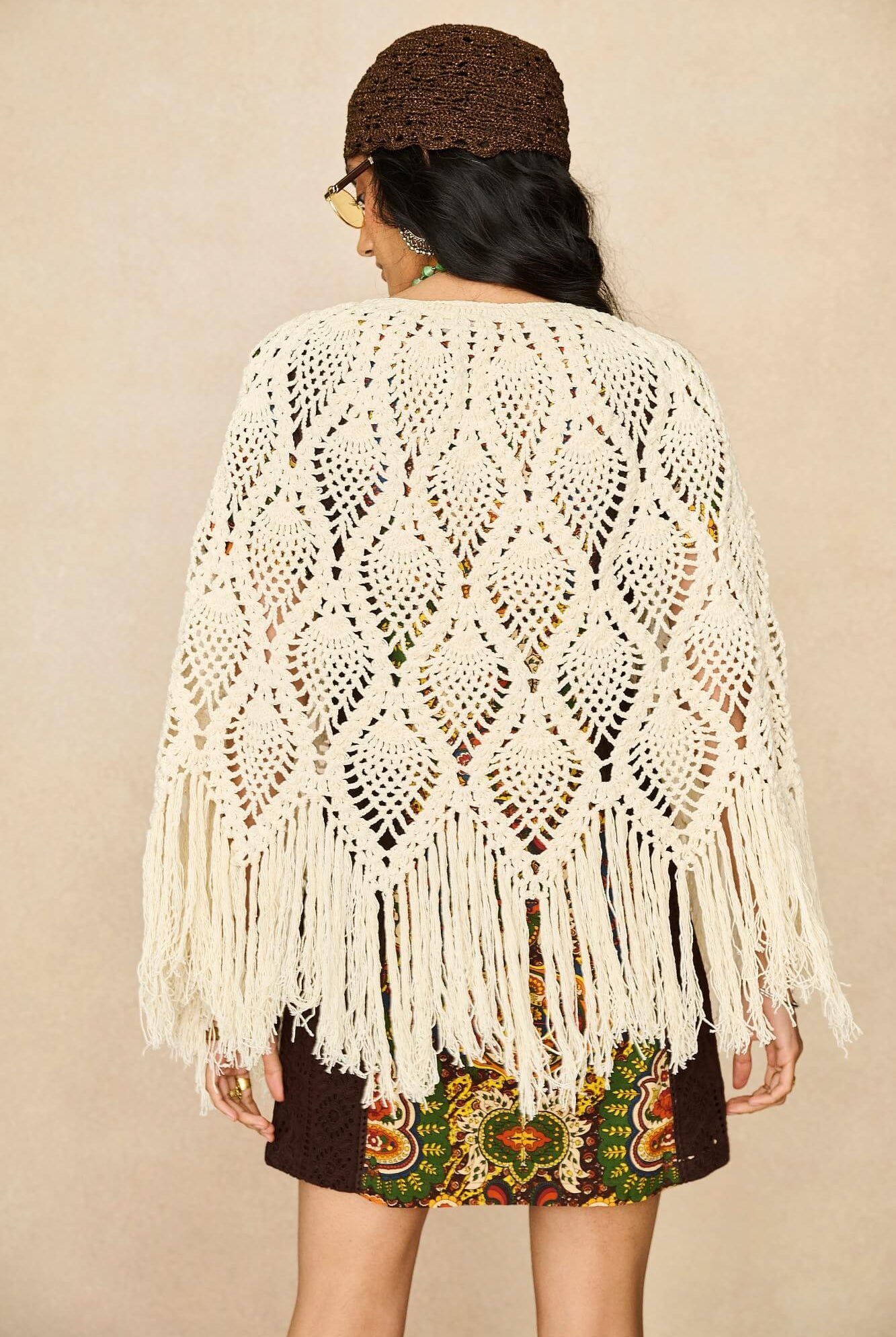Model wearing cream crochet cape with 70s printed mini dress by The Hippie Shake, back view