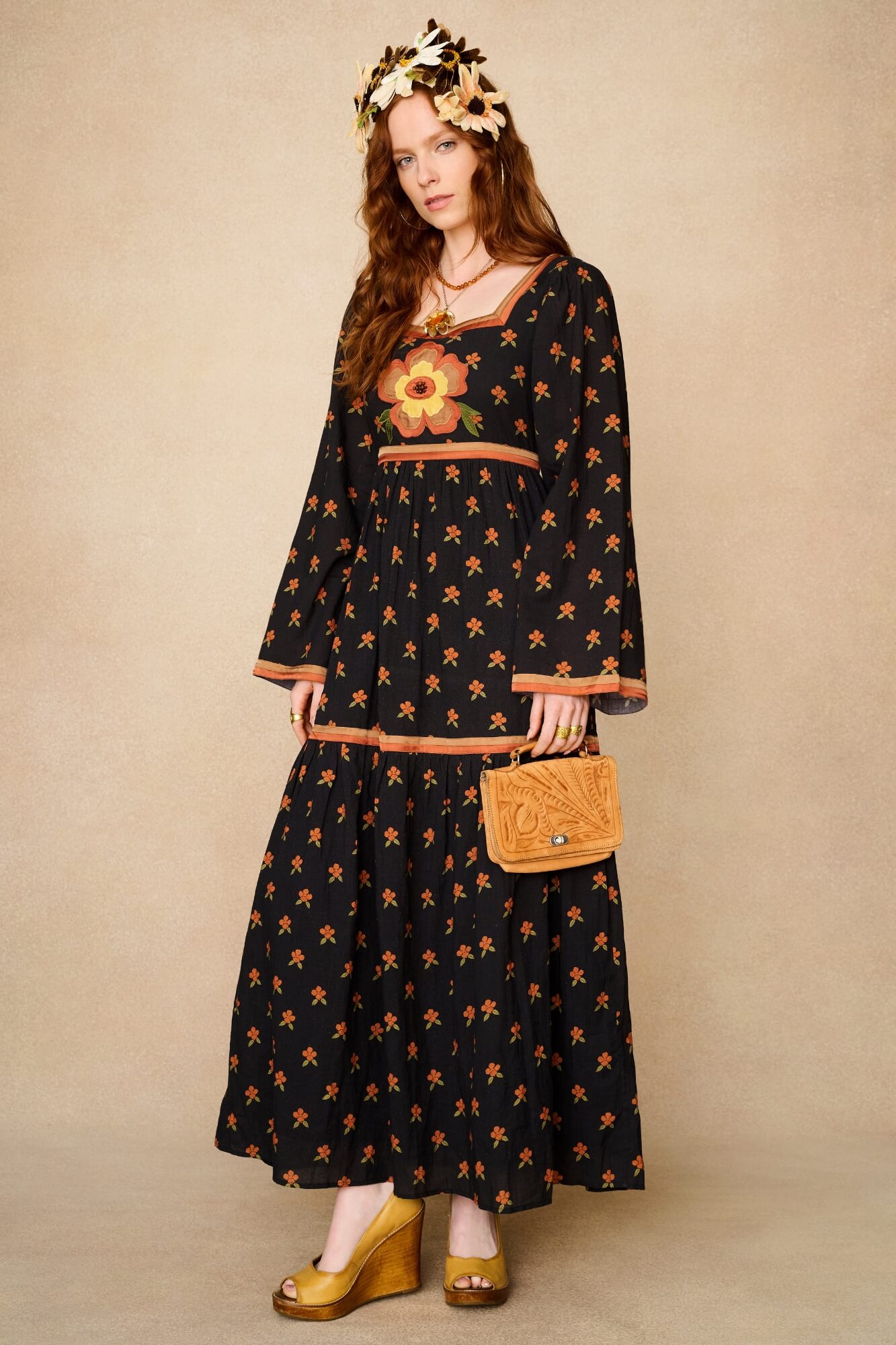 Woman wearing a black dress with floral patterns and holding a matching handbag against a beige background