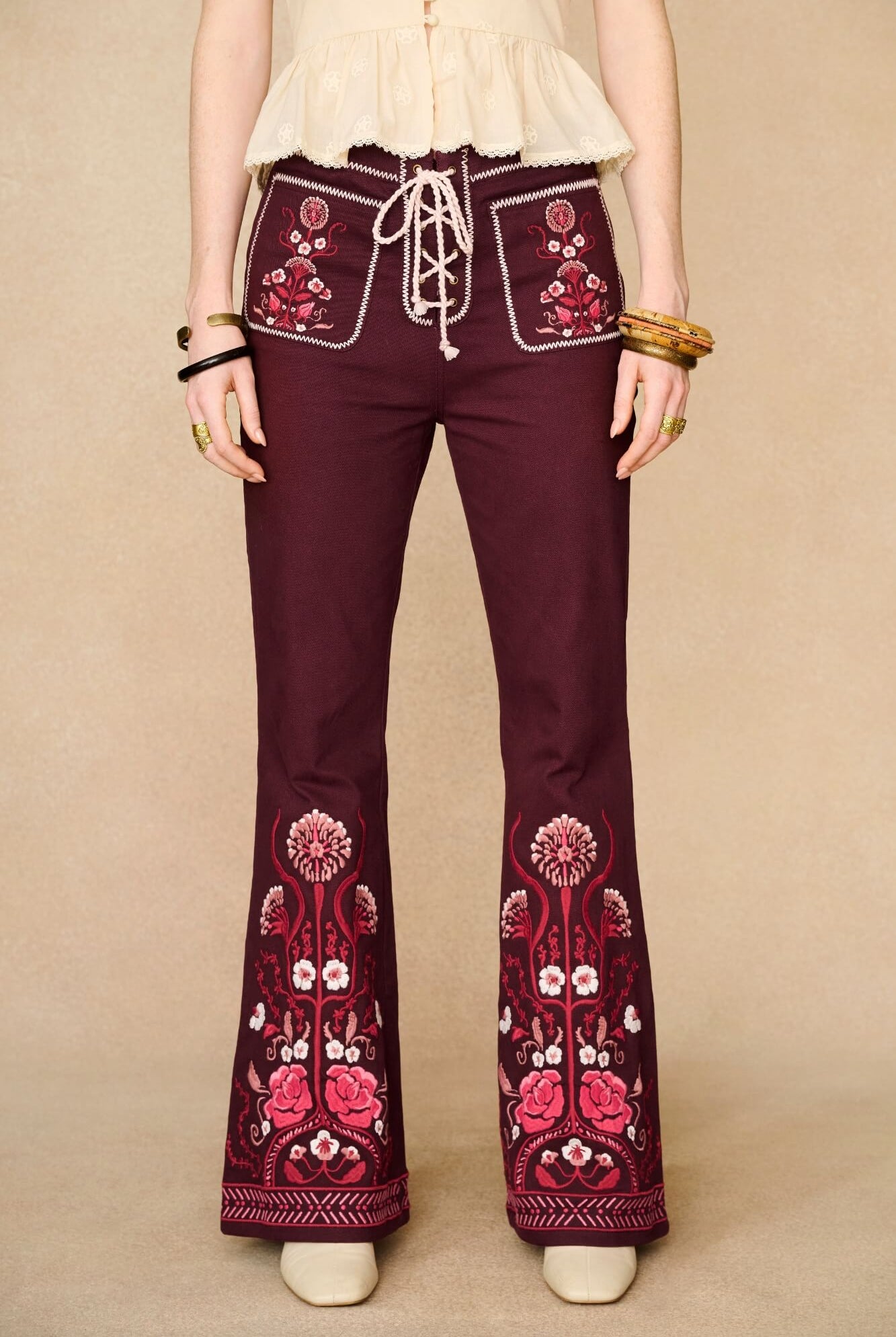 Burgundy 70s bell-bottom pants with floral embroidery on a beige background