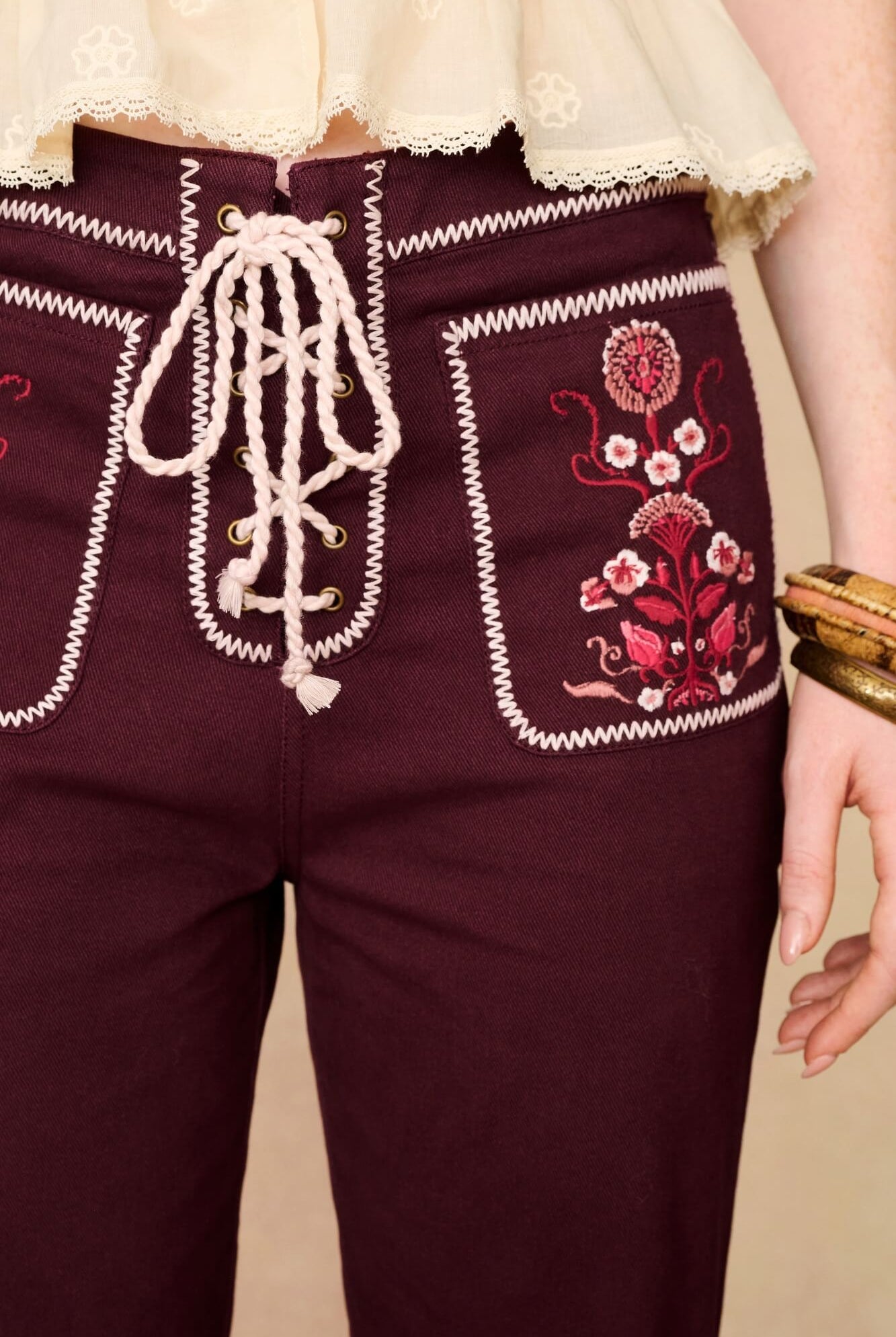 Burgundy pants with white embroidery and floral patterns on a beige background