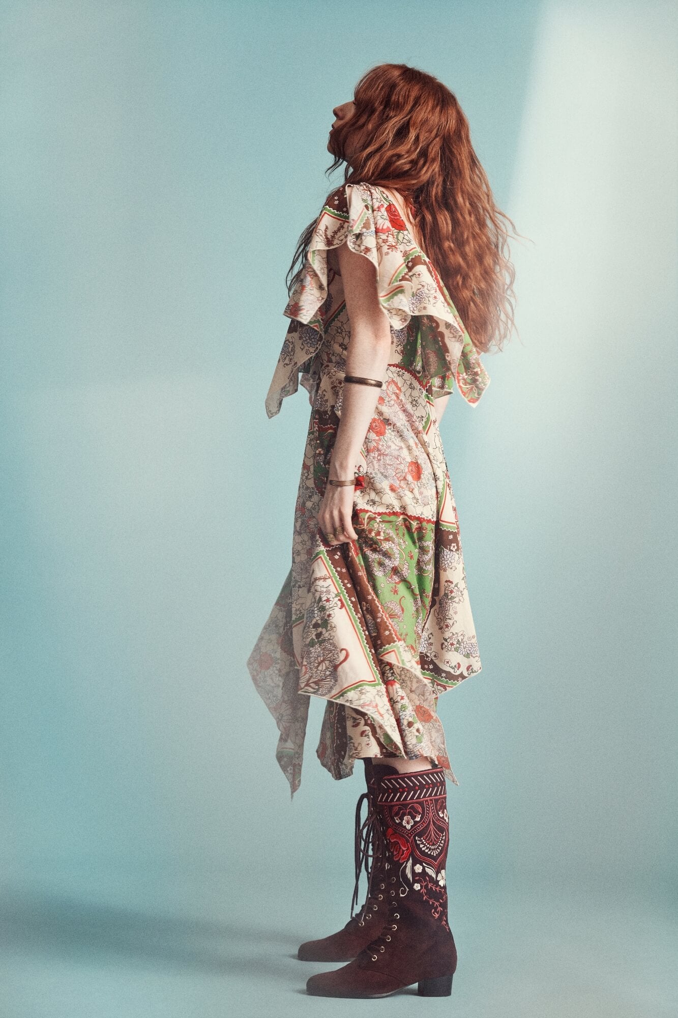 Woman wearing a patterned dress and brown boots against a light blue background