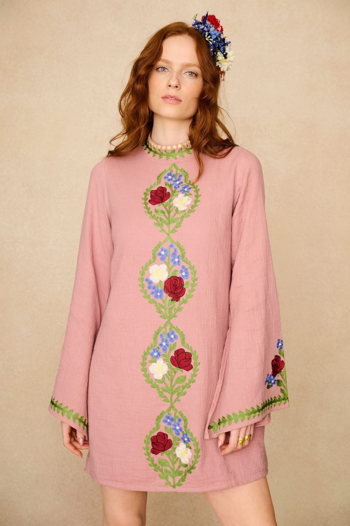 Woman wearing a pink dress with floral embroidery on a beige background
