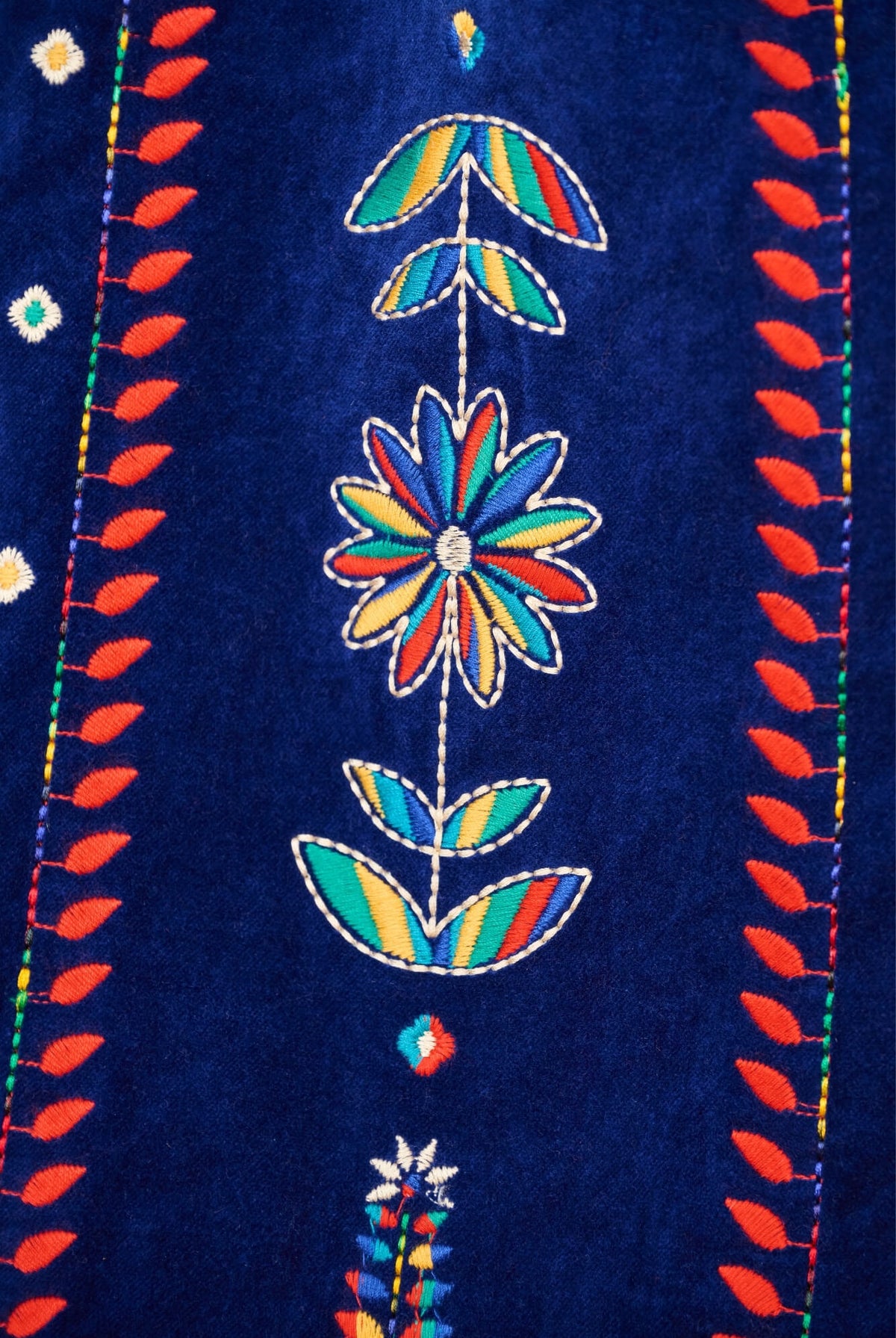 Close-up of a dark blue textile featuring colorful embroidered floral motifs and red leafy border details.
