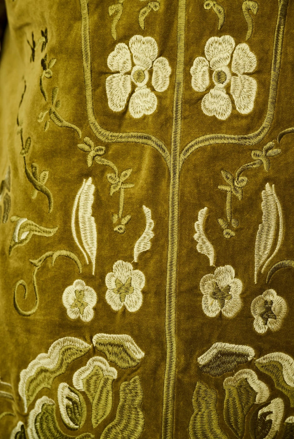 Close-up of an olive green embroidered textile with cream floral and vine motifs.