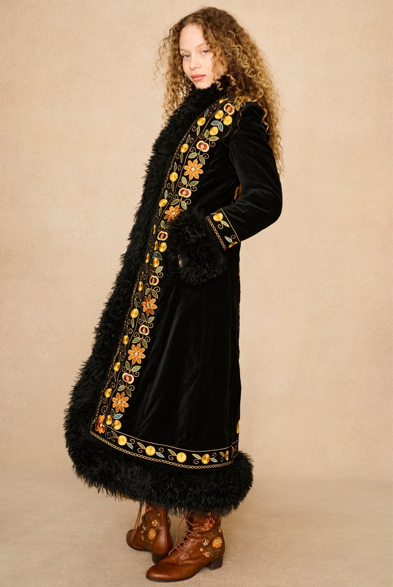 Model wearing long black Penny Lane coat by The Hippie Shake, with faux-fur trip and floral embroidery - side on view