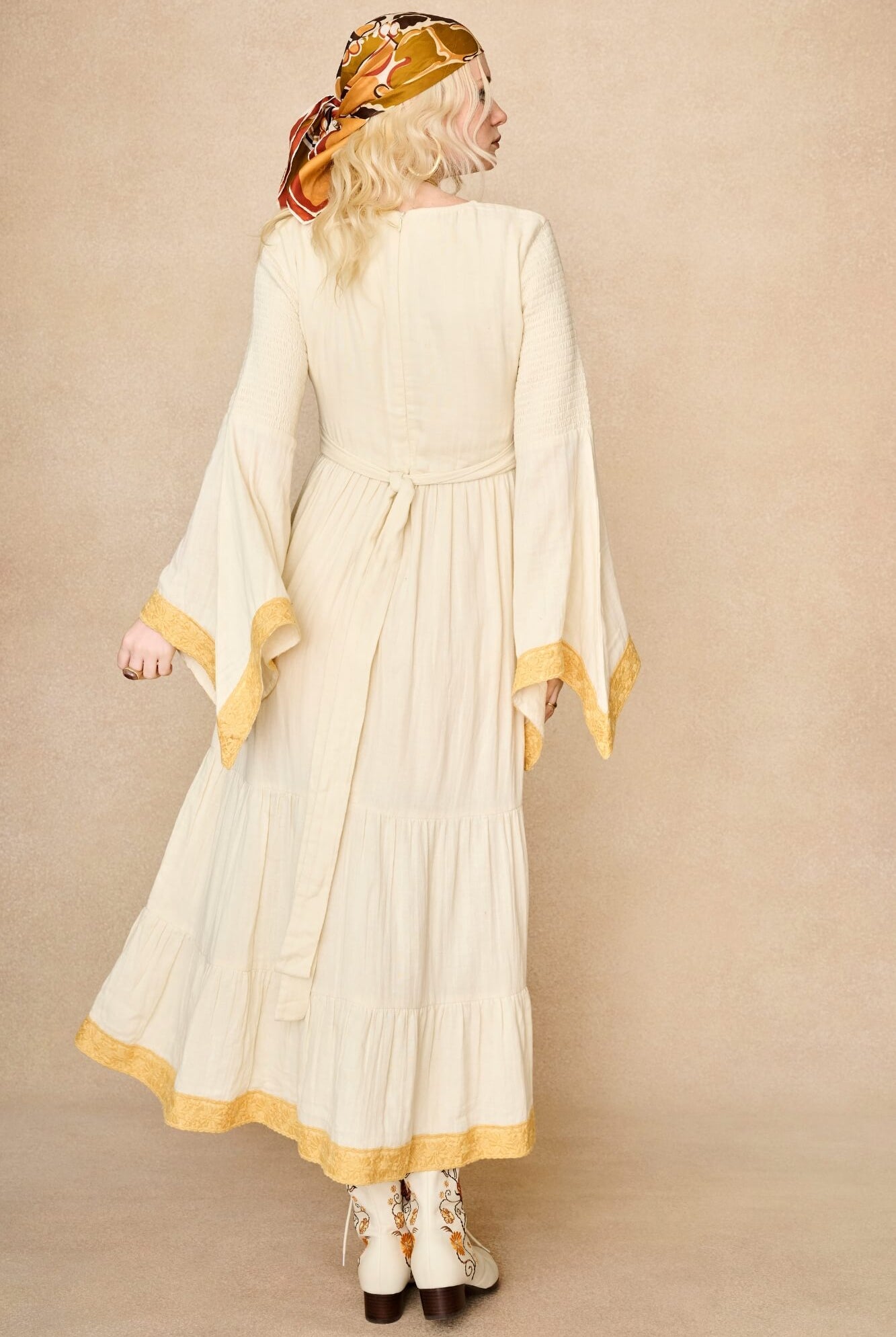Model wearing 70s cream long sleeve maxi dress with lace-up Penny Lane boots by The Hippie Shake, back view