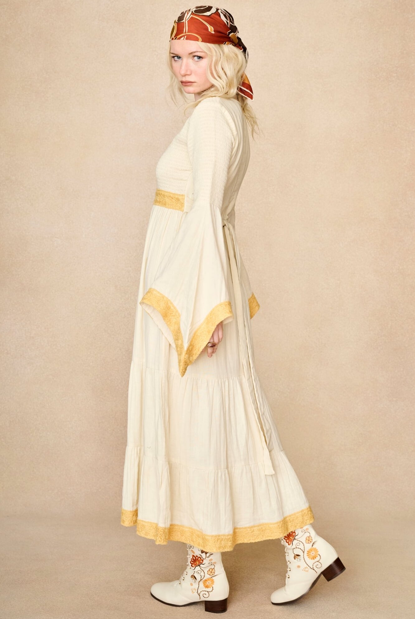 Model wearing 70s cream long sleeve maxi dress with lace-up Penny Lane boots by The Hippie Shake, side view