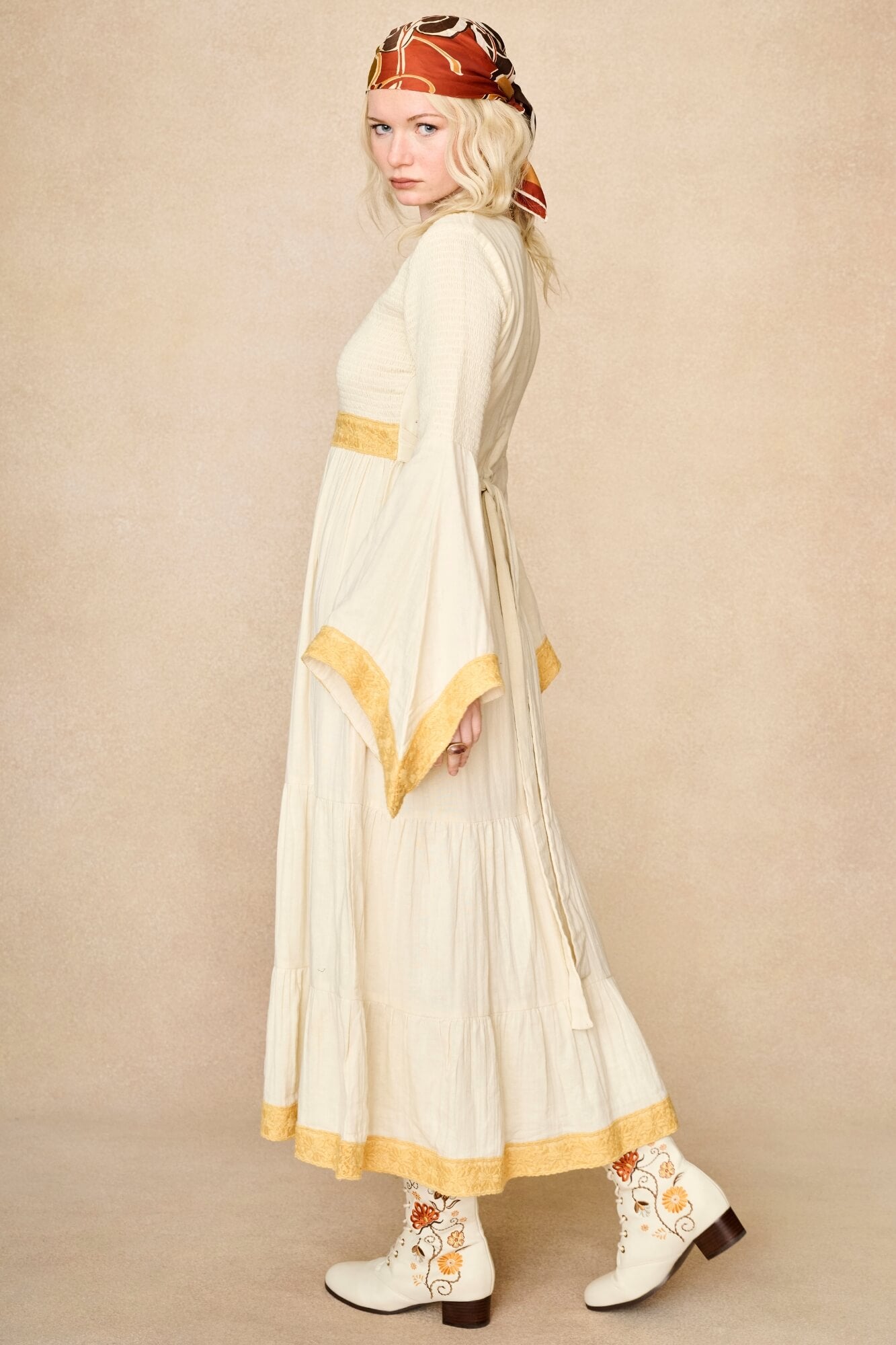 Model wearing 70s cream long sleeve maxi dress with lace-up Penny Lane boots by The Hippie Shake, side view