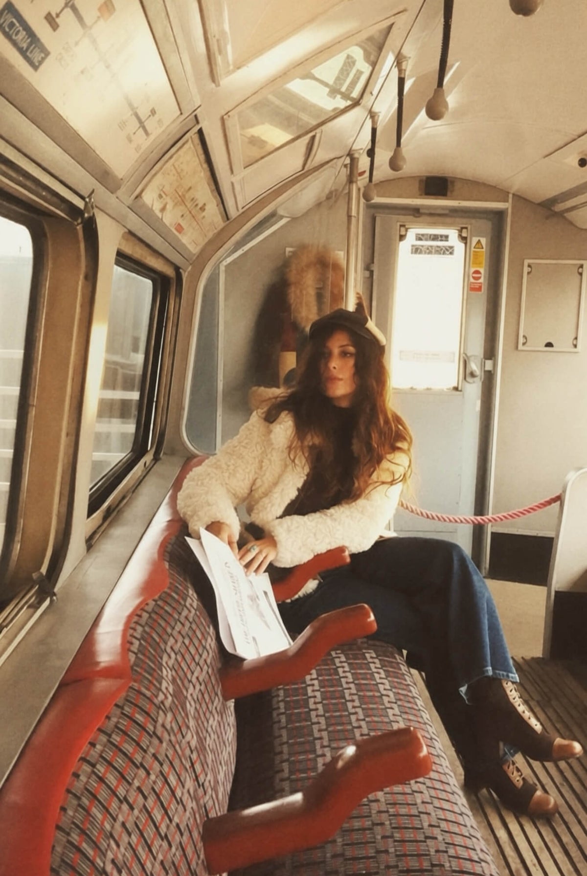 A woman inside a London tube train wearing a shaggy cream 70s jacket paired with denim flares and boots.
