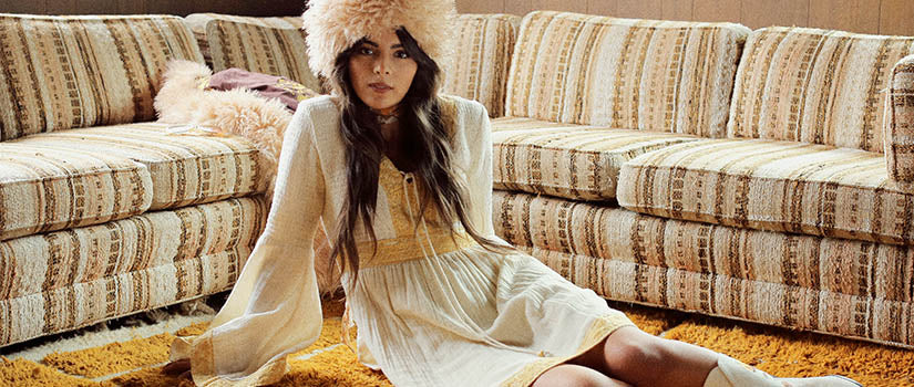 Hero banner for The Hippie Shake's embroidered and bohemian dresses - Model sits on floor wearing white dress.