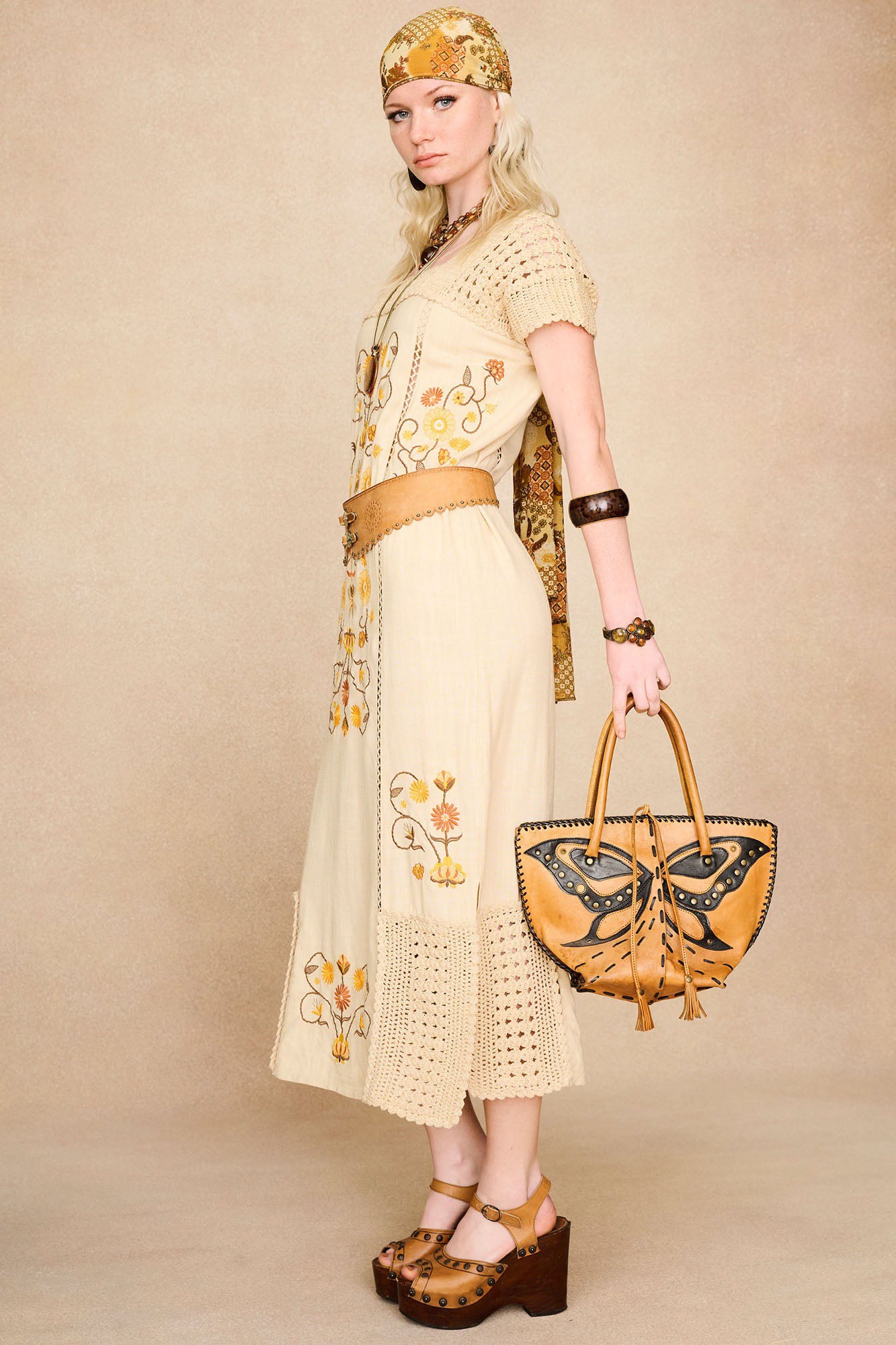 Side view of The Hippie Shake's 70s inspired cream crochet trim midi dress styled with a statement belt. and butterfly bag.