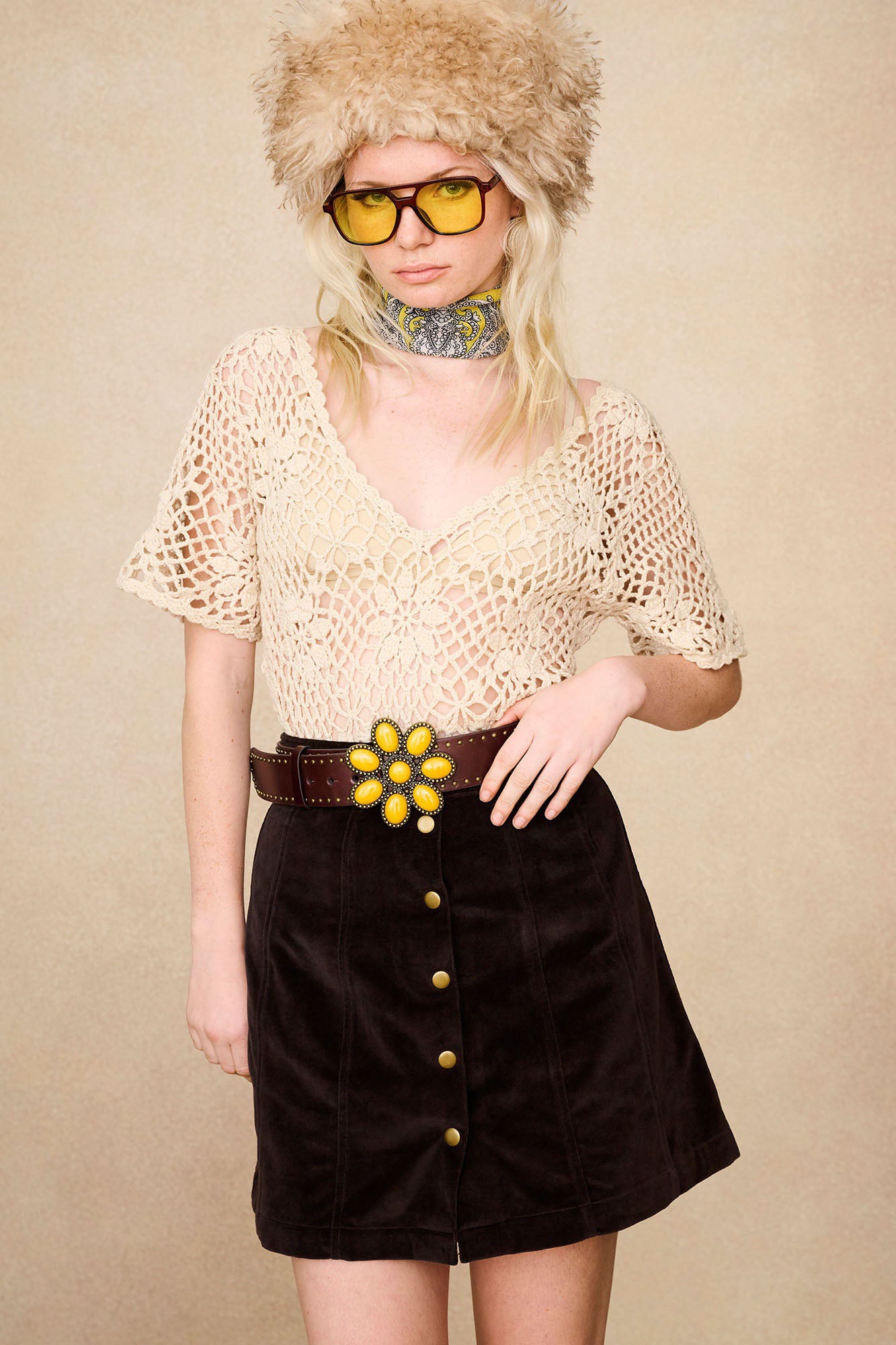 Model wearing The Hippie Shake's brown velvet mini skirt with crochet top and yellow floral buckle belt.