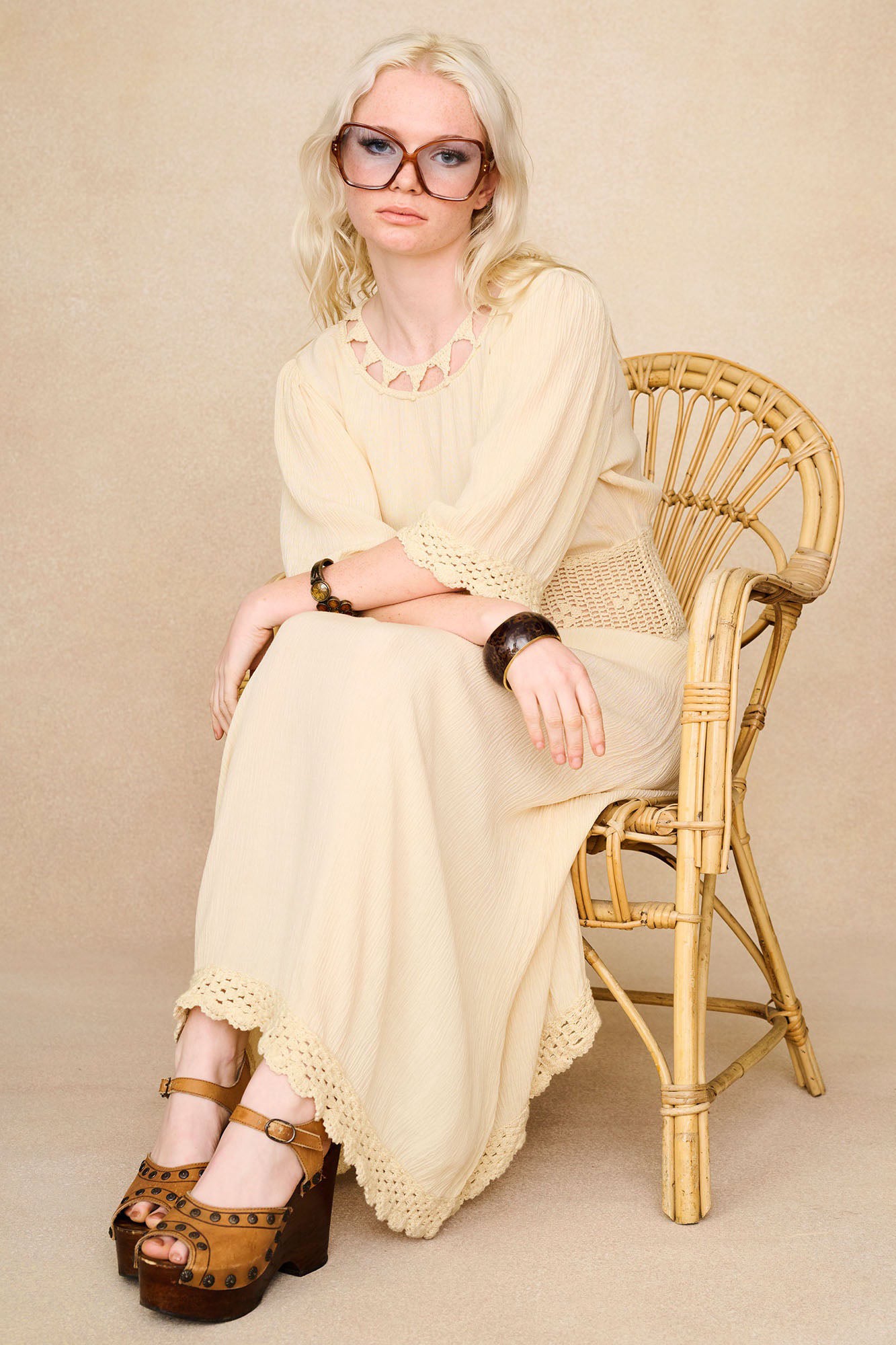 Model in chair wearing The Hippie Shake's cream crochet midi dress with retro jewellery