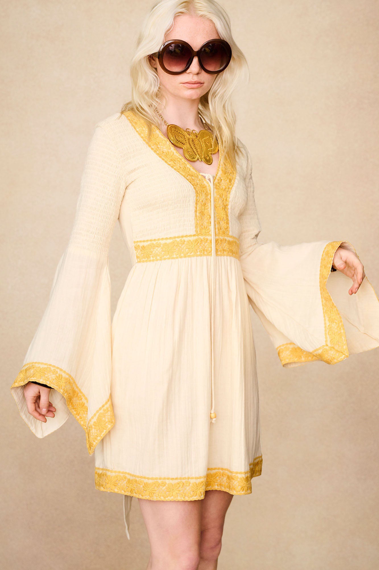 Side view of The Hippie Shake's cream lace trim mini dress with fluted sleeves and yellow lace detail.