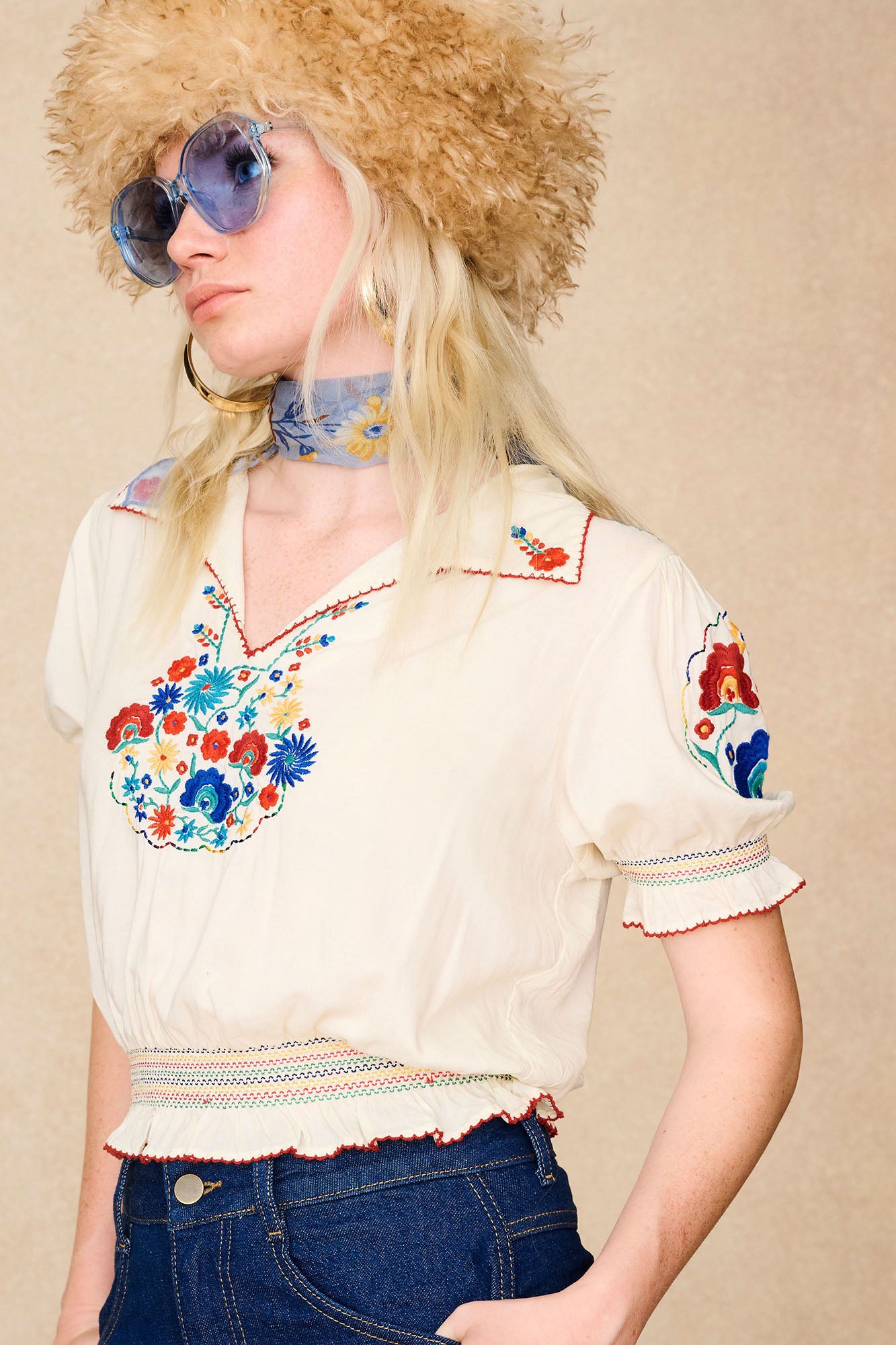 Side view of model in The Hippie Shake's brown faux fur hat with blue sunglasses, styled with our floral embroidered cream blouse.