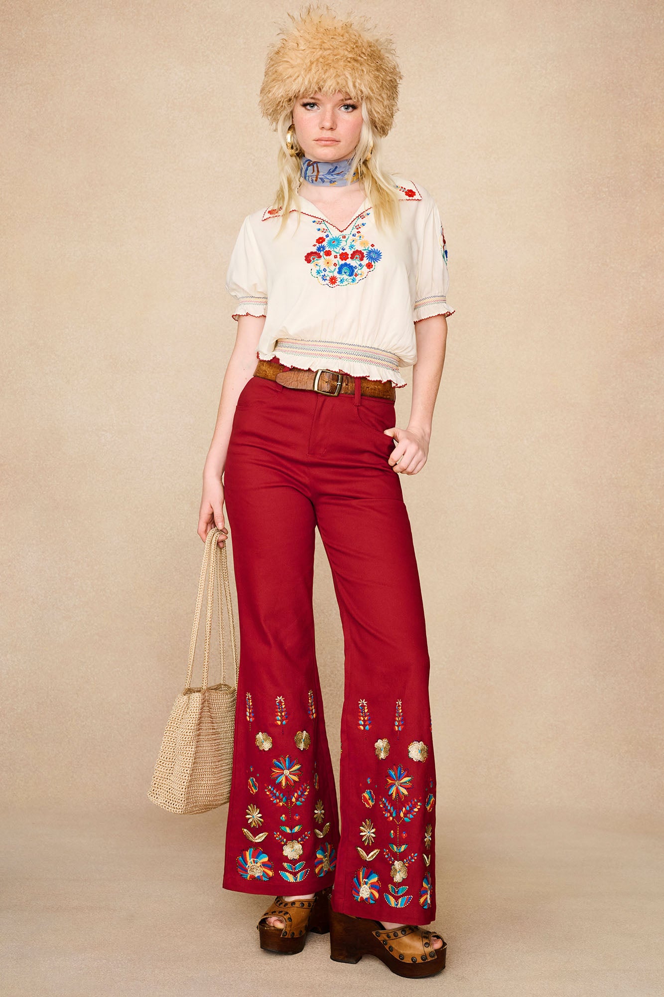 Model wearing The Hippie Shake's red embroidered flared trousers styled with a cream peasant blouse and faux fur hat.