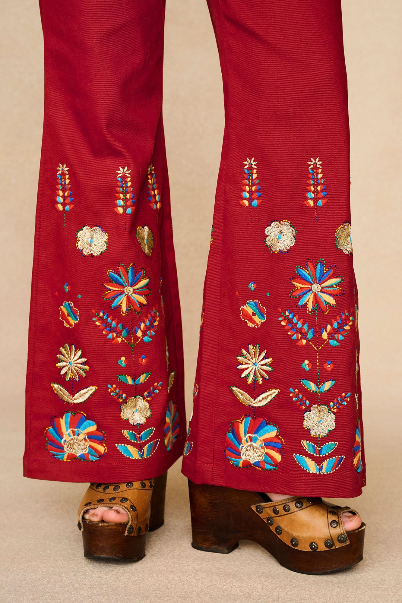 Close-up of The Hippie Shake's red embroidered flared trousers showing detailed gold and multicolour floral embroidery.