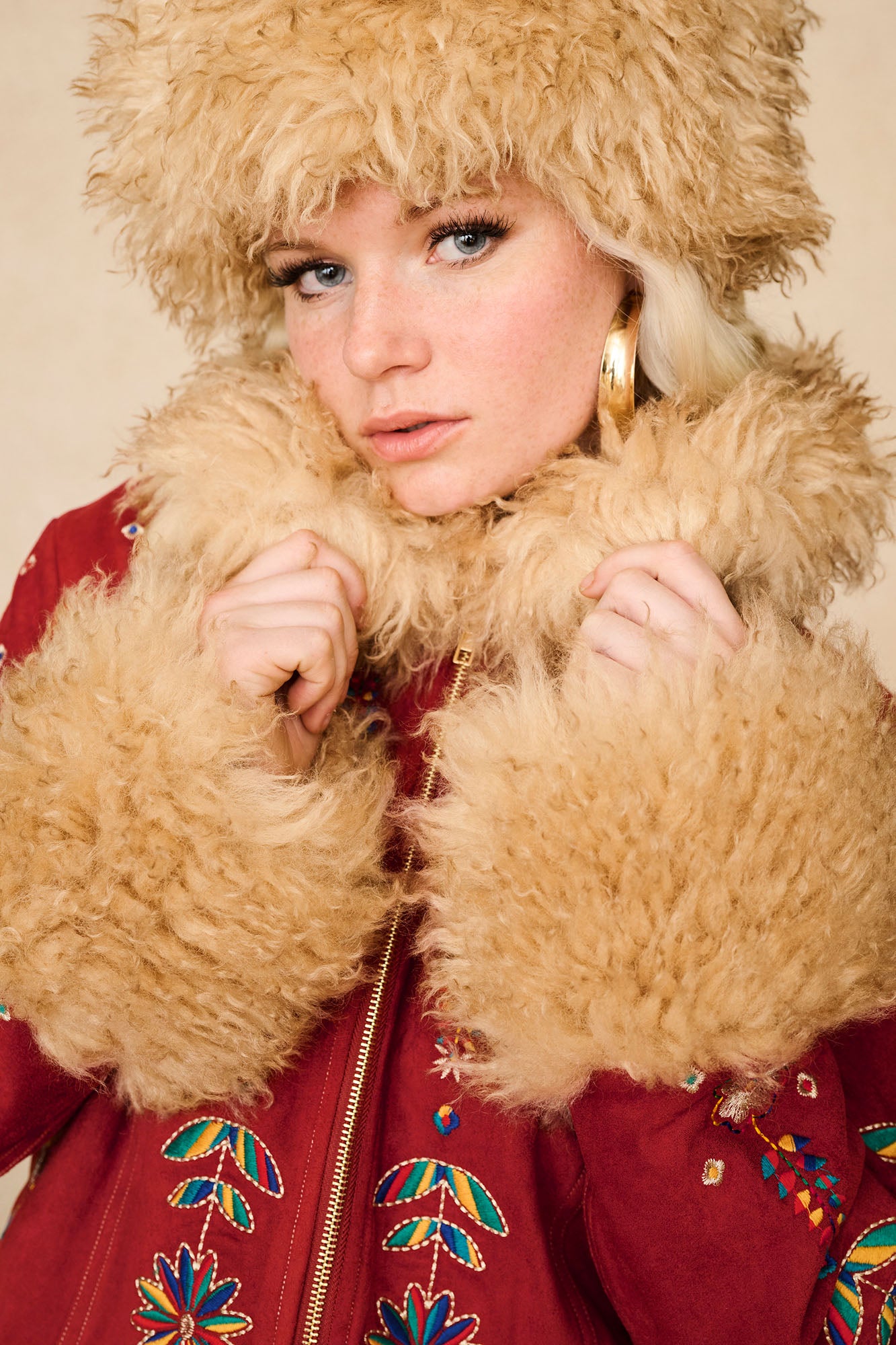 Close-up of model in The Hippie Shake's 70s inspired brown faux fur hat styled with our red Penny Lane coat and gold hoops.