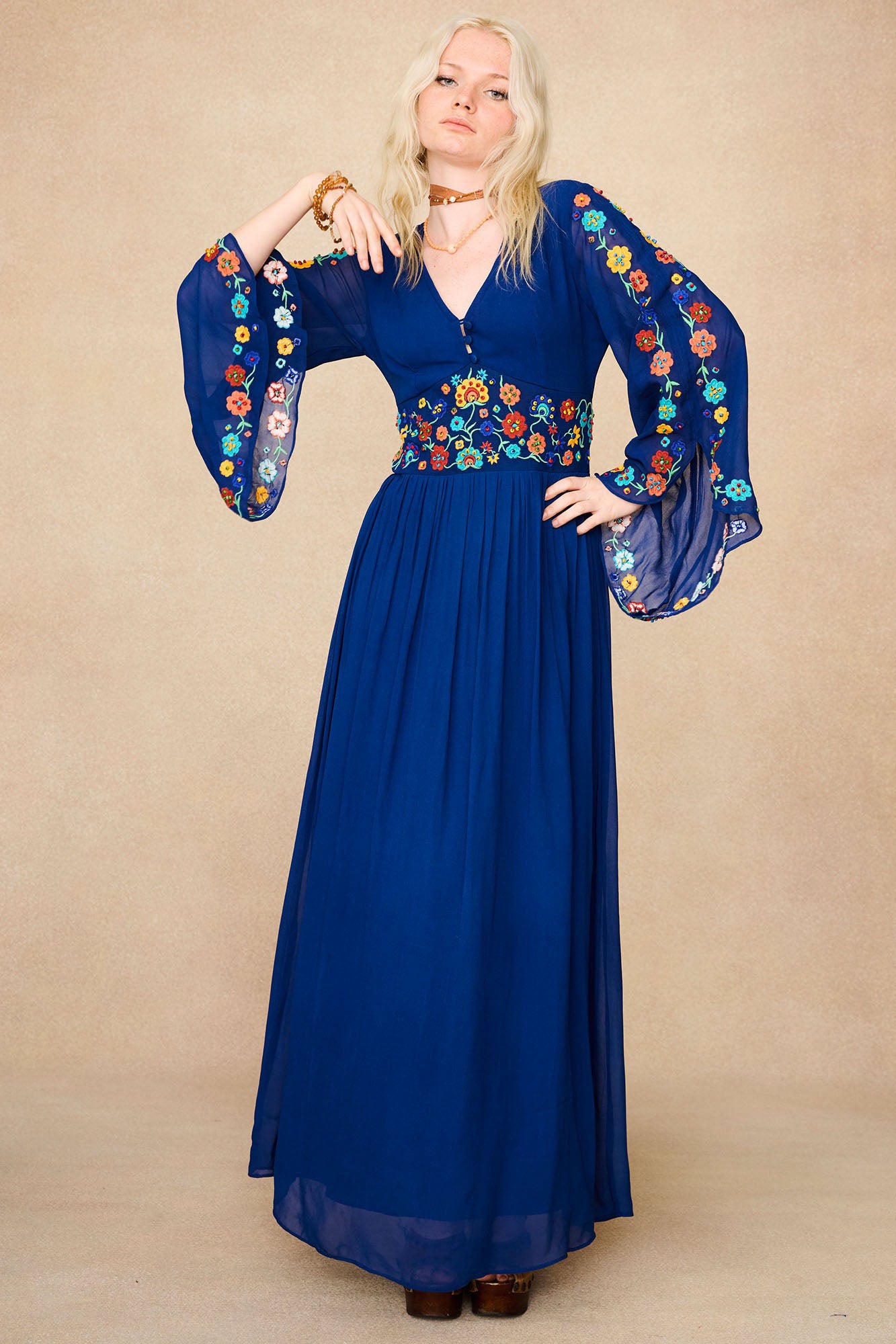 Model wearing The Hippie Shake's blue vintage embroidered maxi dress with flared sleeves and floral detailing on bodice and arms.