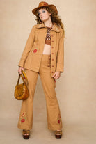 Woman wearing a 70s style brown halter top with embellishments and high-waisted pants against a beige background - front view with suit set