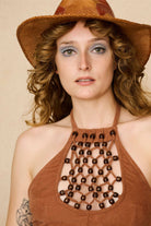 Woman wearing a 70s style brown halter top with embellishments and high-waisted pants against a beige background - close view