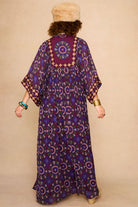 Model wearing a 70s style bohemian maxi dress in a printed purple fabric with hand embroidery - back view