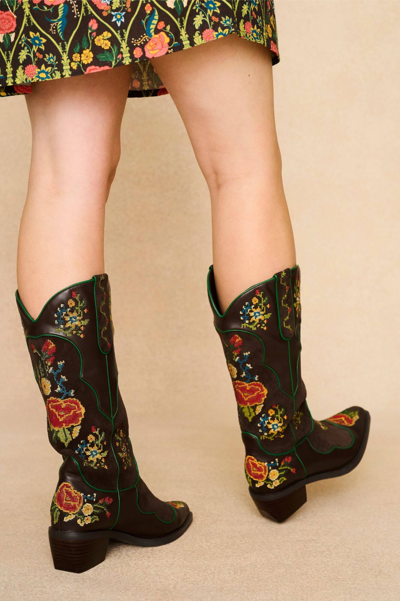 Brown Western style embroidered boots with floral patterns worn by a model on a beige background - back view
