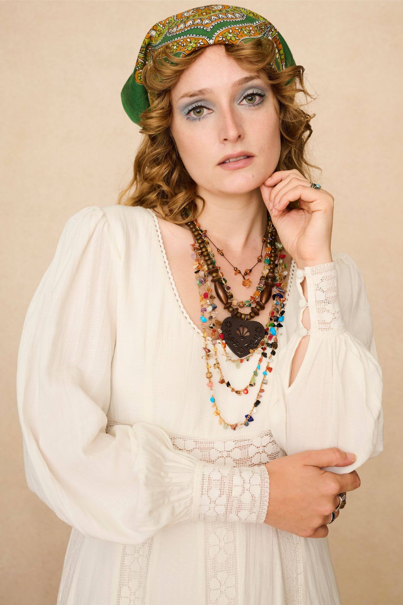 Woman in a long cream lace floaty 70s style maxi dress against a beige background - close up with jewellery