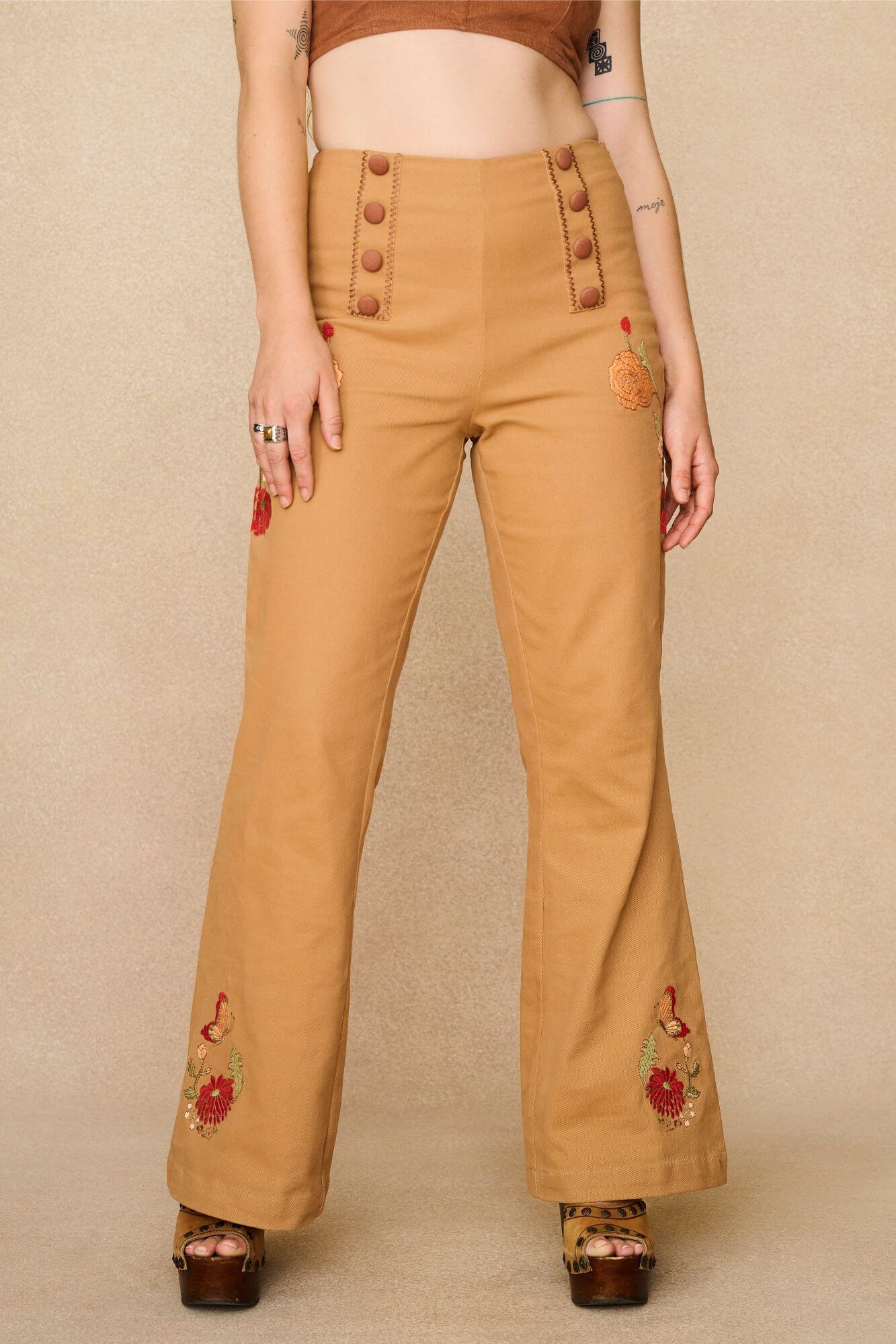 Tan-coloured 70s style trousers with floral embroidery on a beige background - front view