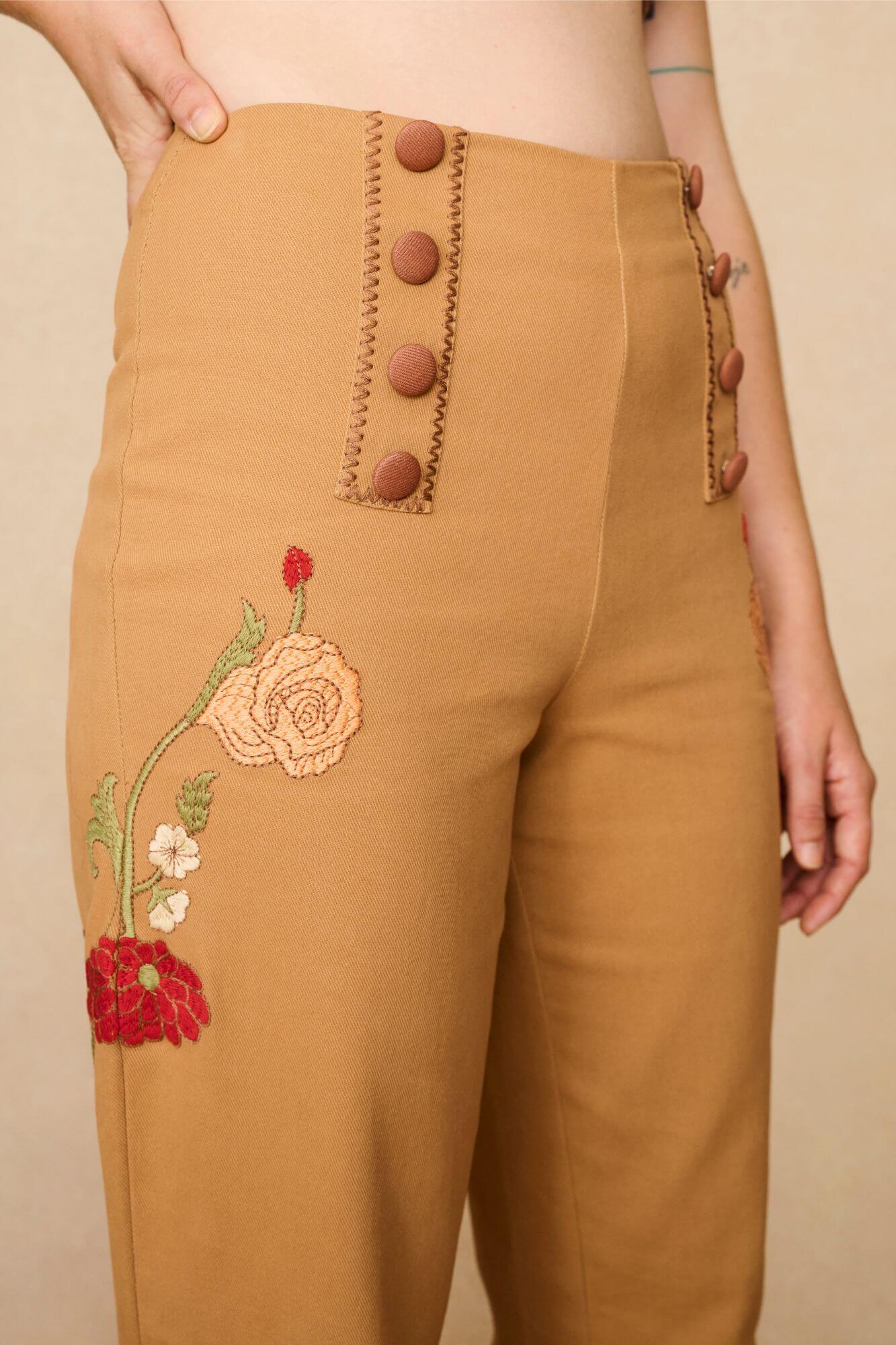 Tan-coloured 70s style trousers with floral embroidery on a beige background - close up of embroidery