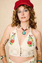 Woman wearing a red cap, floral embroidered top, and colourful necklace against a beige background - close up front view